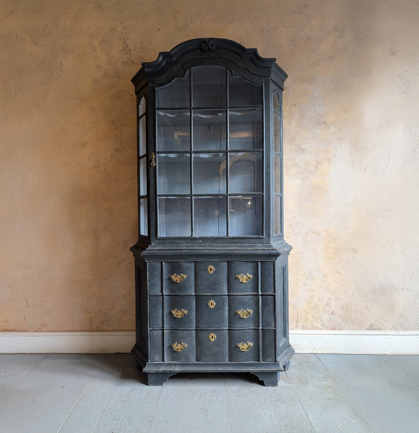 Dark wooden cabinet with glass panels and drawers against a beige wall.